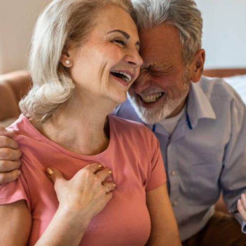 Close up of senior couple at home, laughing and using phone